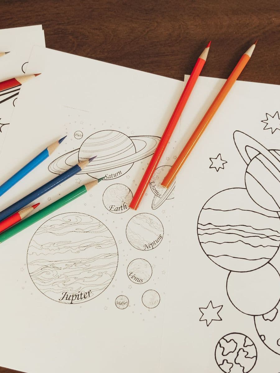 Printed planet coloring pages with Saturn and Jupiter outlines beside red, orange, blue and green pencils