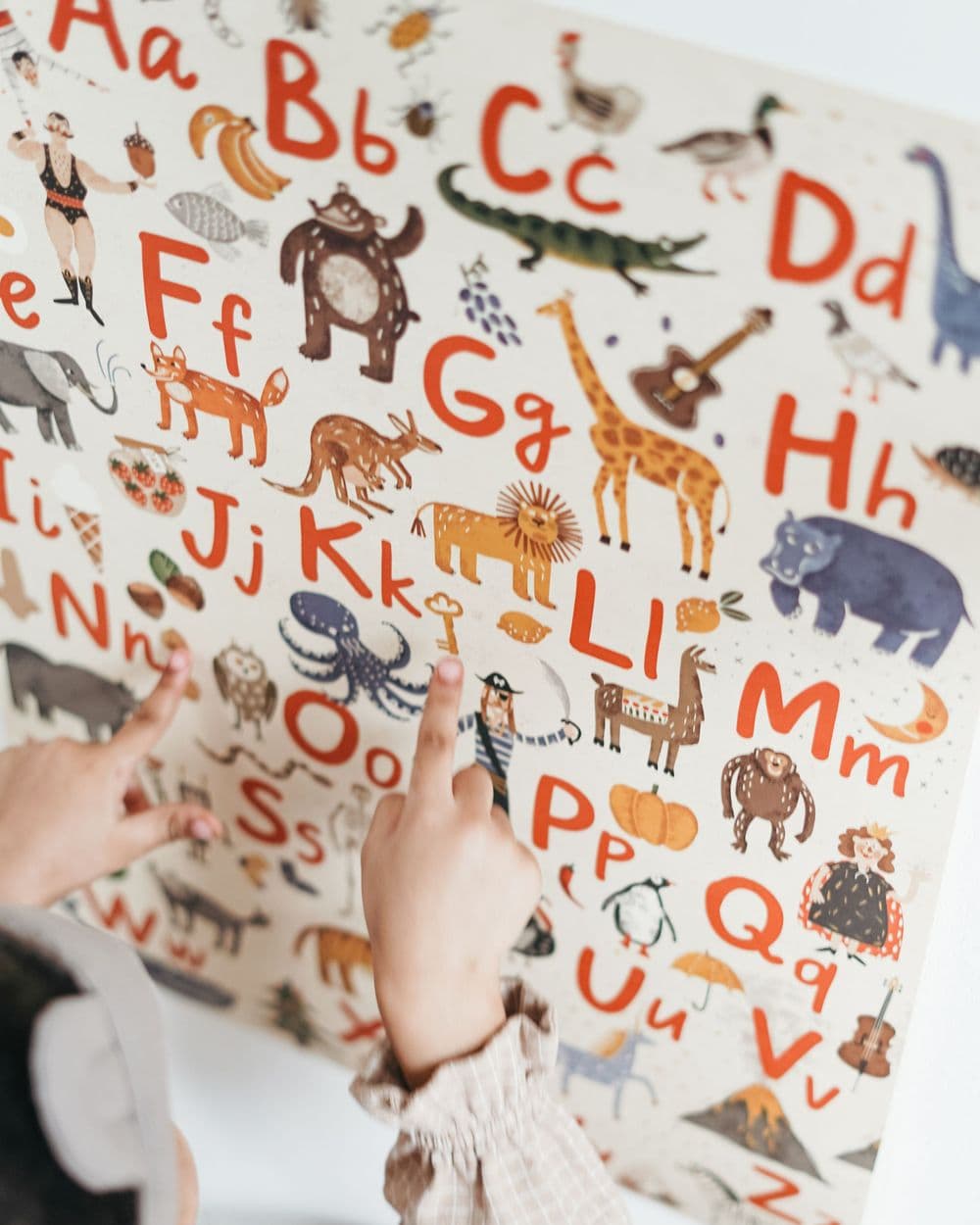 Illustrated alphabet poster with animals and hand-lettered letters, a child pointing at it