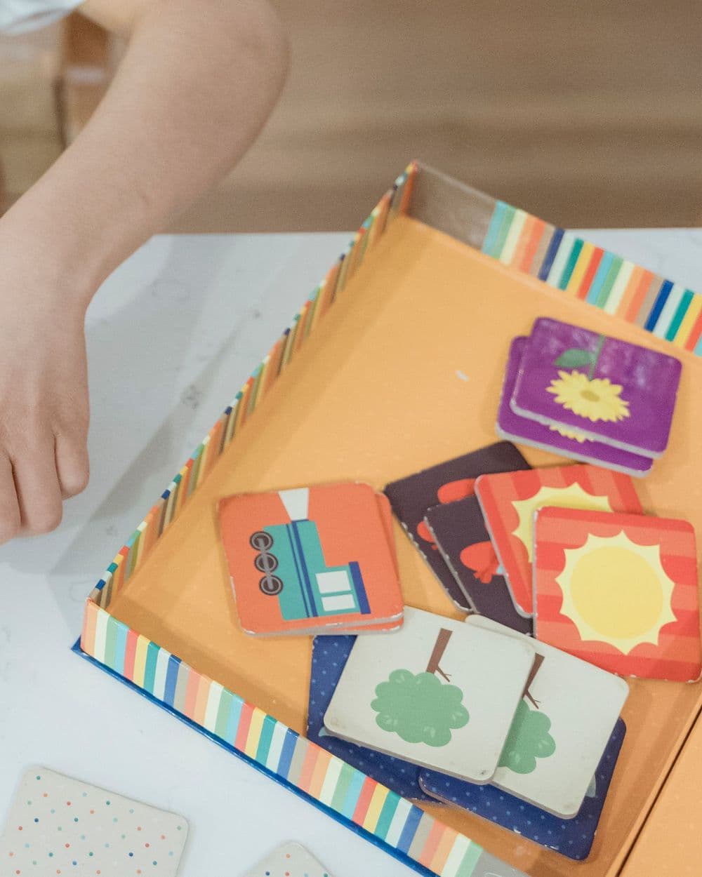Illustrated matching cards with suns, flowers and trees in a striped game box