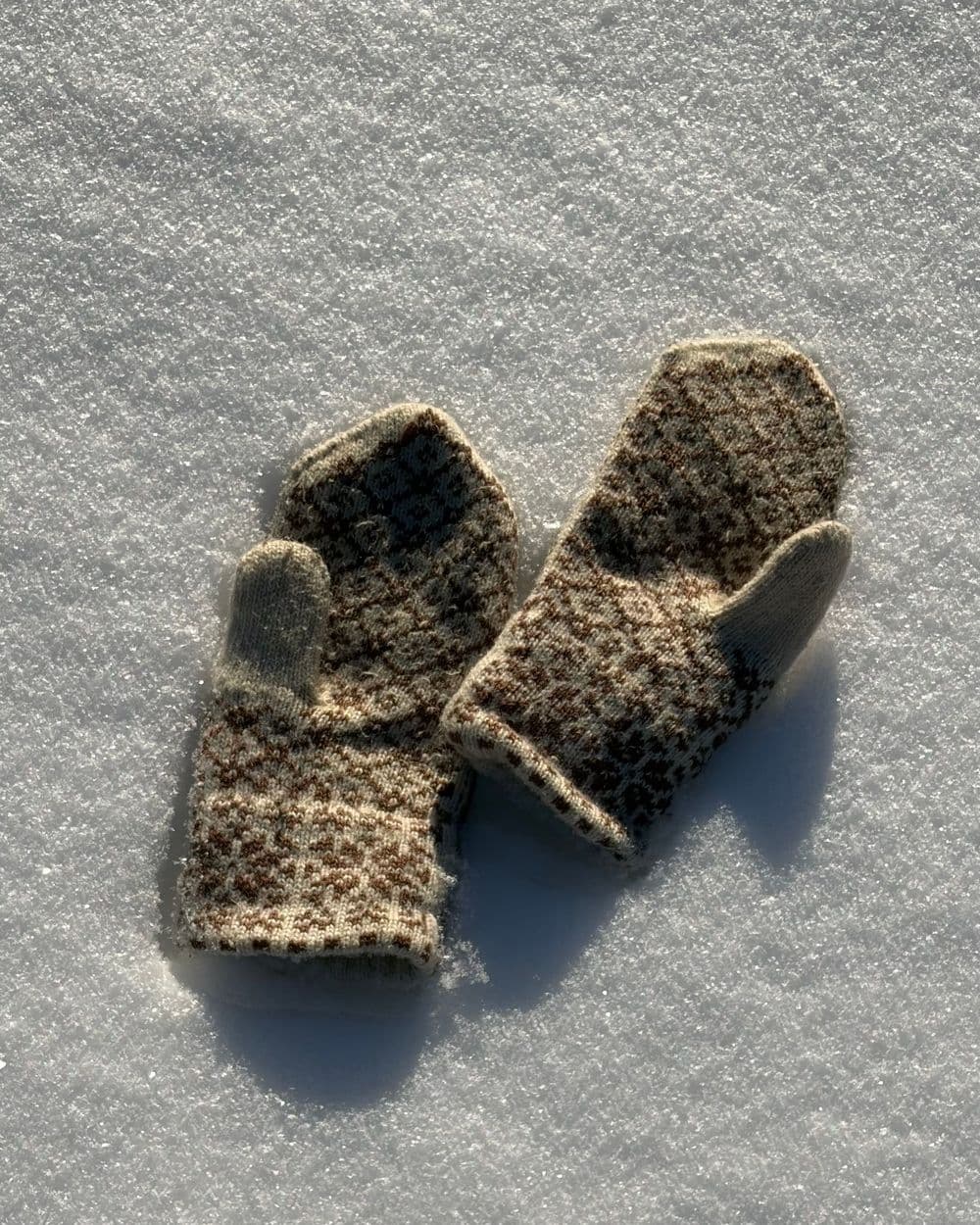 Pair of patterned wool mittens lying on fresh white snow