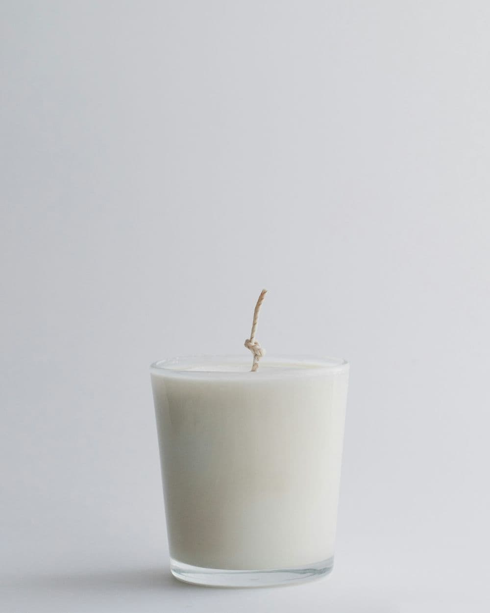 White soy candle in a clear glass jar on a light grey background