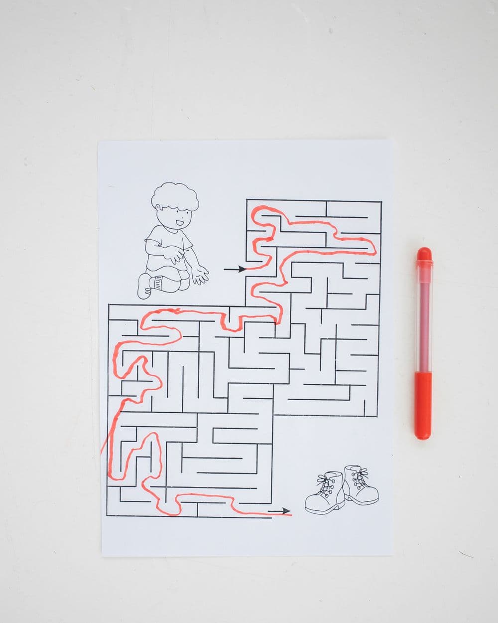Printed maze activity sheet traced in red marker next to a red pen on a white desk