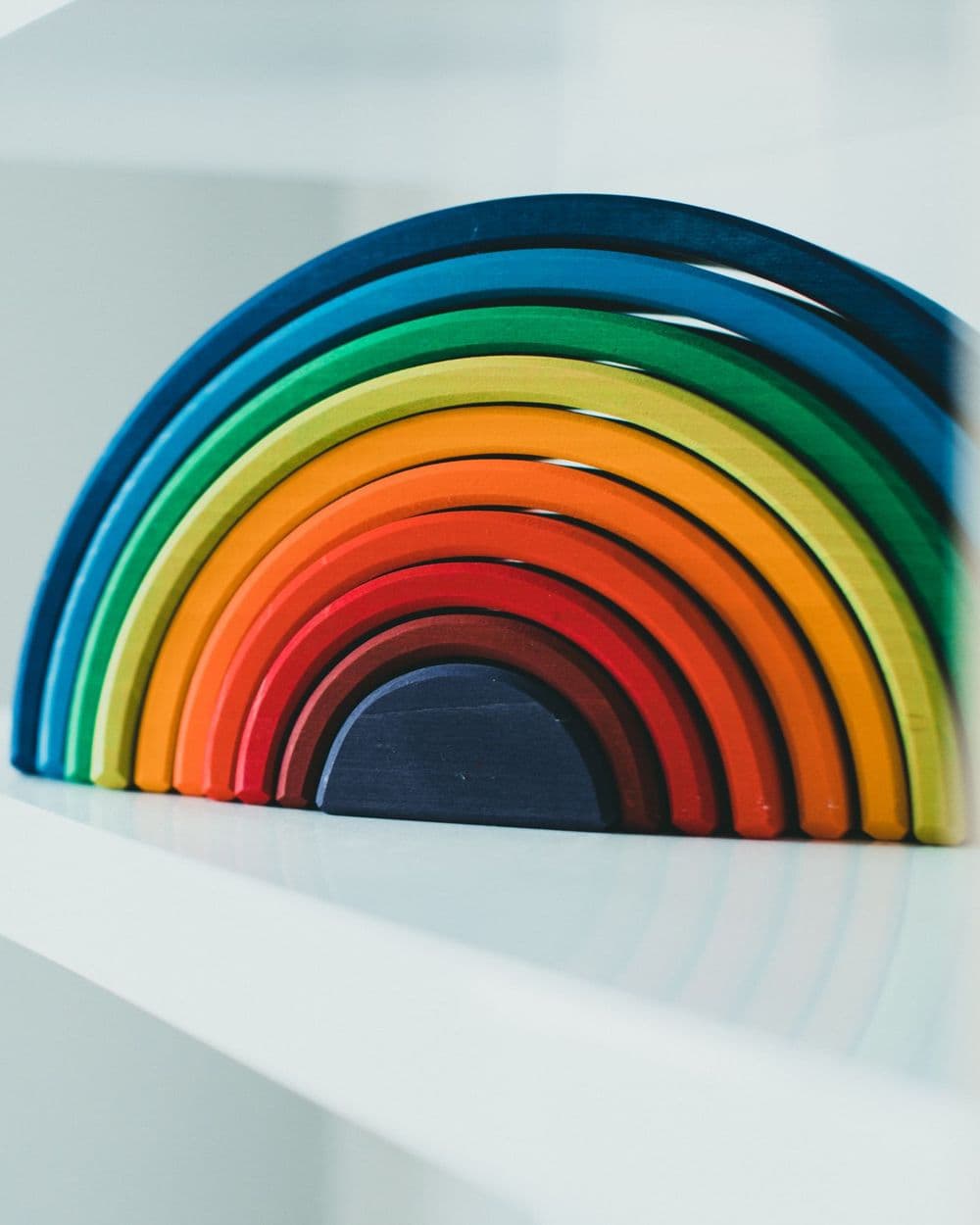 Wooden rainbow stacking toy in bright colors on a white shelf