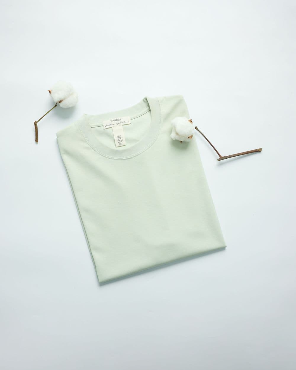 Folded mint green cotton t-shirt with cotton bolls on a light background